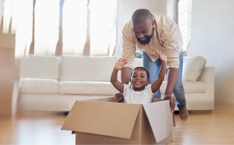 A father pushes his young child across the floor in a moving box