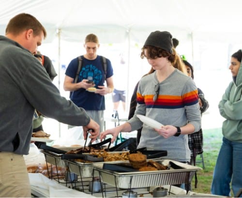 a young person helps themselves to food at an outdoor event inside a large tent