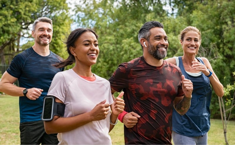 A group of adults jogging together in a park wearing headphones and smart devices